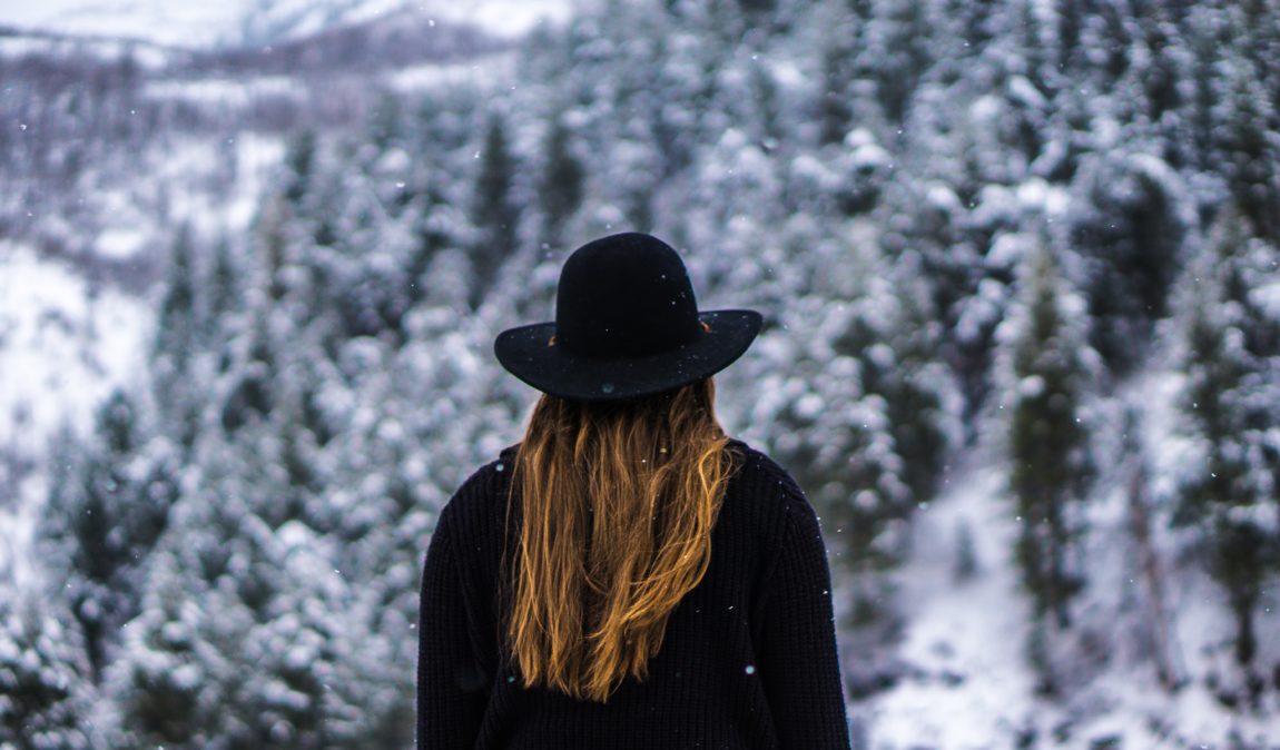woman in black hat and sweater looking at snowy trees