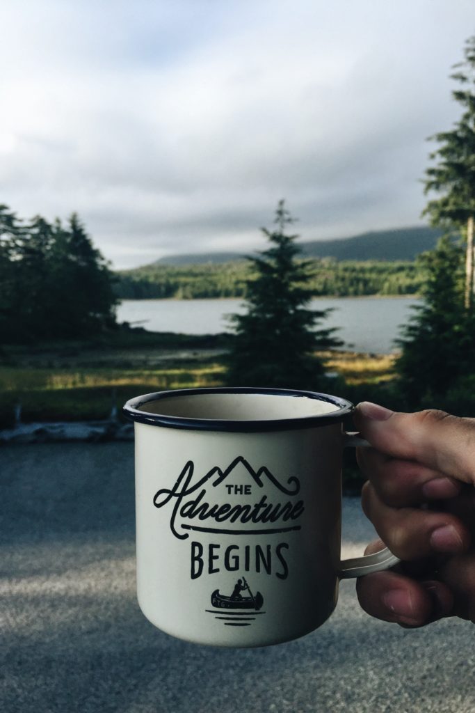 In the forest holding a mug that says the adventure begins