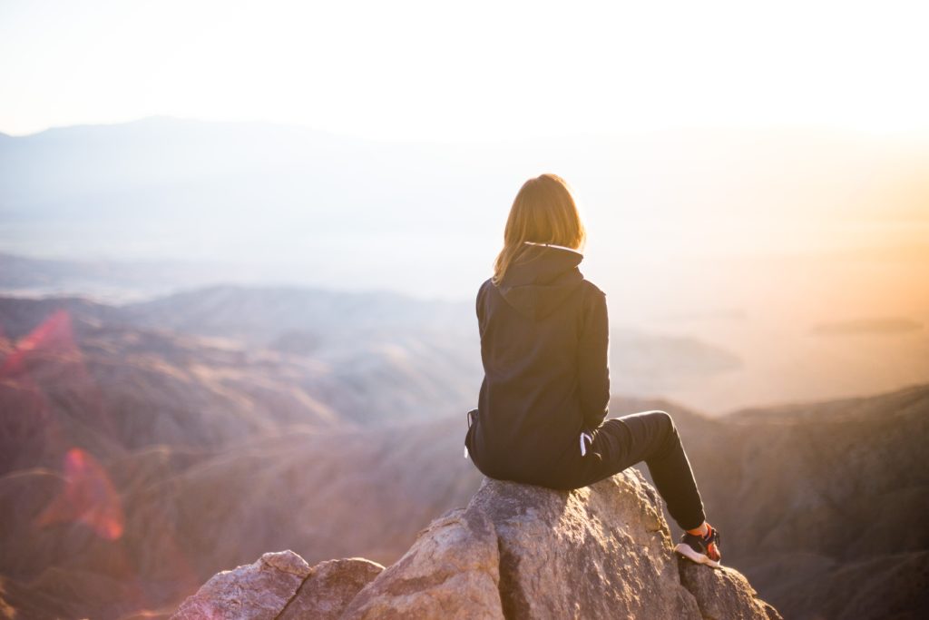 a young woman sits on a rock gazing out at the vista of mountains