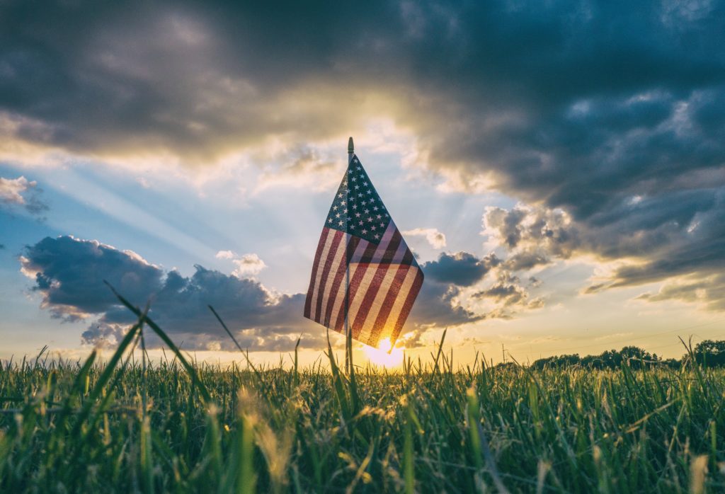 The American flag flying in a field with the sun behind it