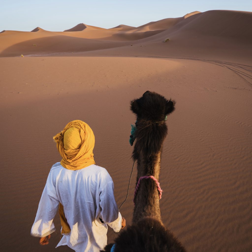 a man walking with a camel in the desert