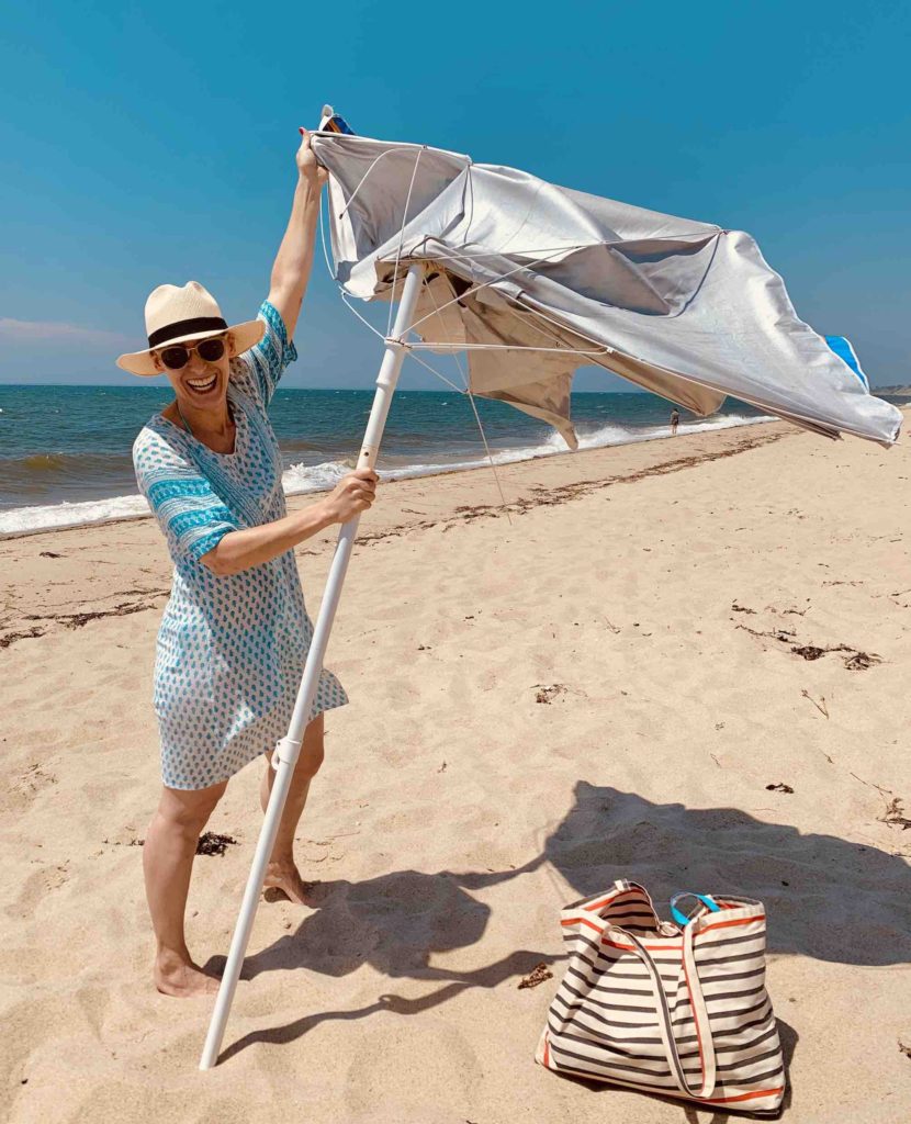 what-to-bring-to-the-beach-merry-trying-to-fix-an-umbrella